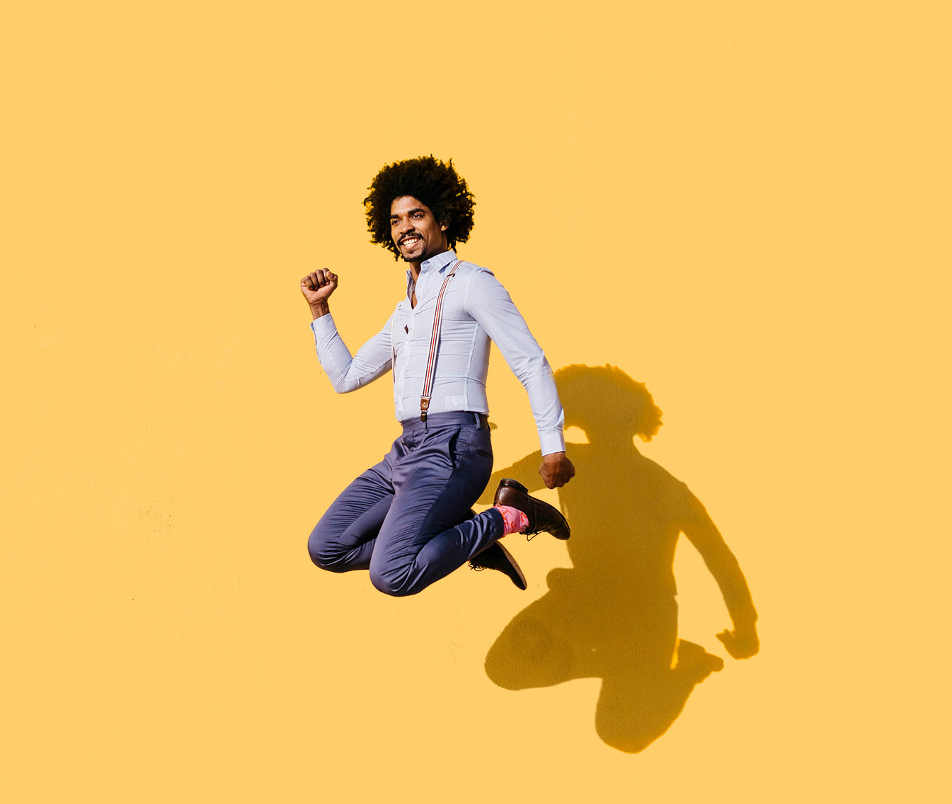 A man in suspenders jumping in the air behind a yellow background